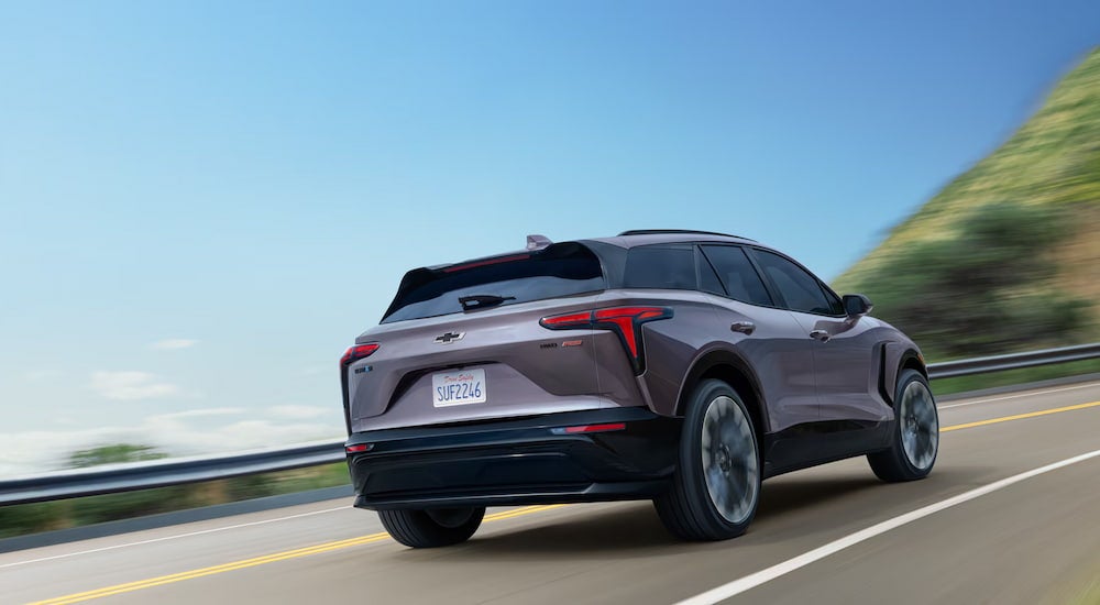 Rear view of a grey 2025 Chevy Blazer EV driving up an open road.
