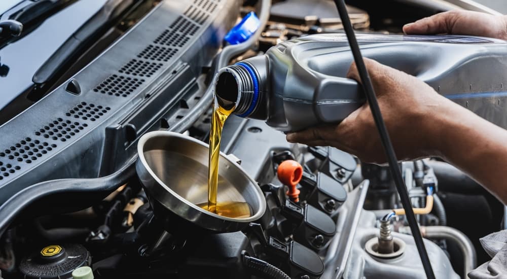 An oil can being poured into a funnel over an engine.