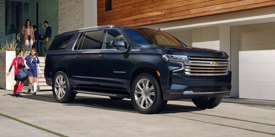 Children in soccer uniforms running beside a dark blue 2026 Chevrolet Suburban SUV