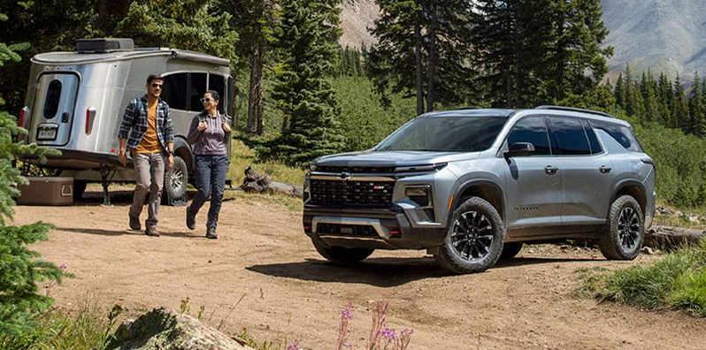 A 2026 Chevy Traverse parked on a dirt road with a camper in the back.