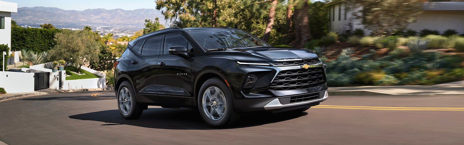 Black 2026 Chevrolet Blazer driving on a curvy road with a scenic background.