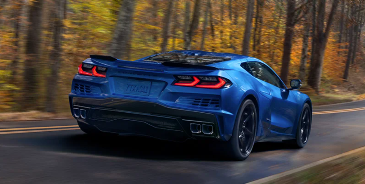 A sleek blue sports car Corvette-E-Ray drives on a winding forest road with autumn foliage. The scene conveys speed and freedom, with vibrant colors and motion.