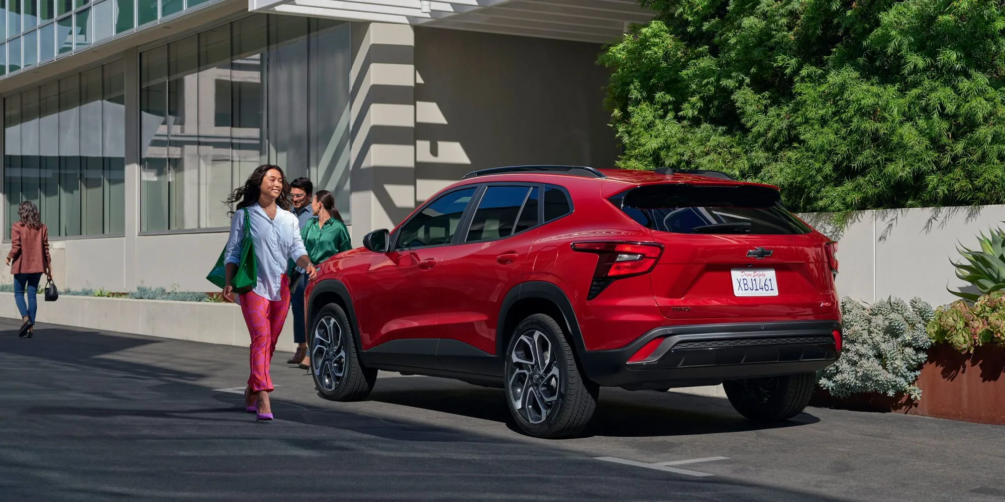 A shopper walking past a red Chevrolet Trax outside a modern building