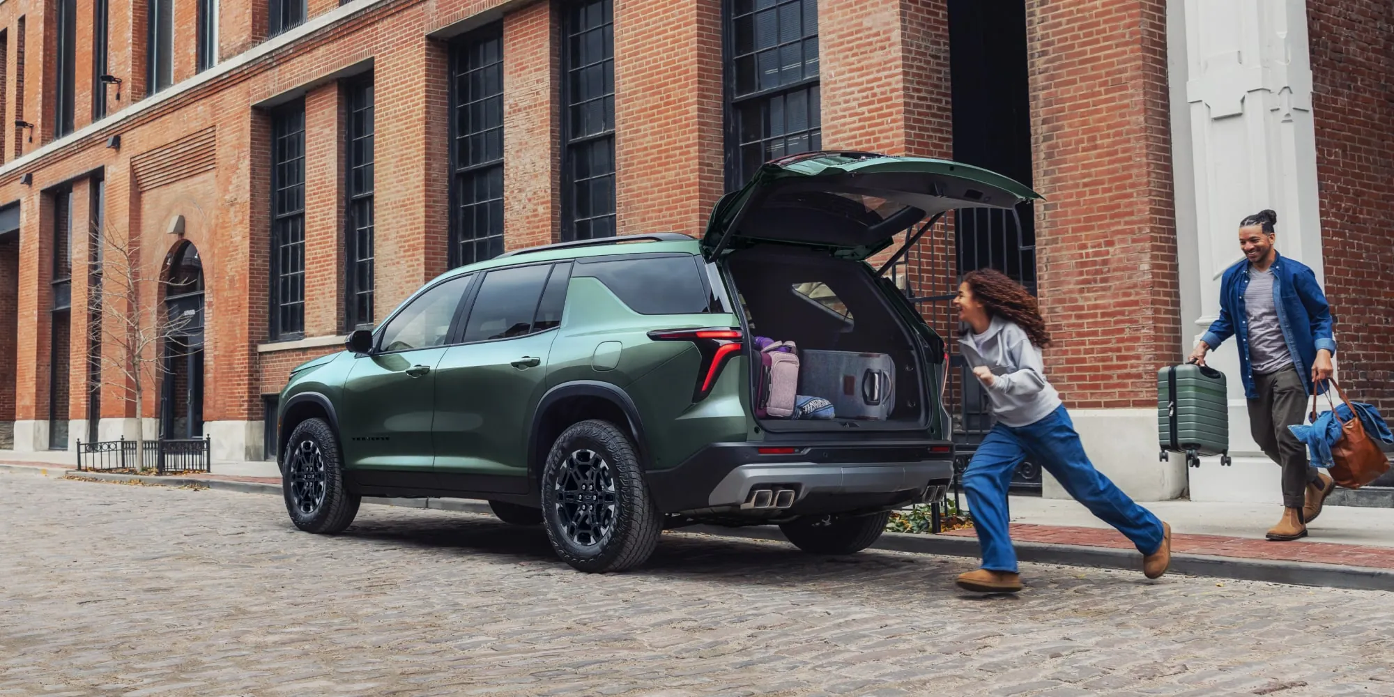 Family loading luggage into a Chevrolet Traverse on a brick street
