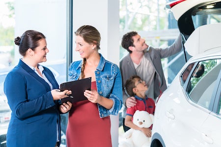 Family buying new car in auto dealer showroom, the sales lady shows the price list
