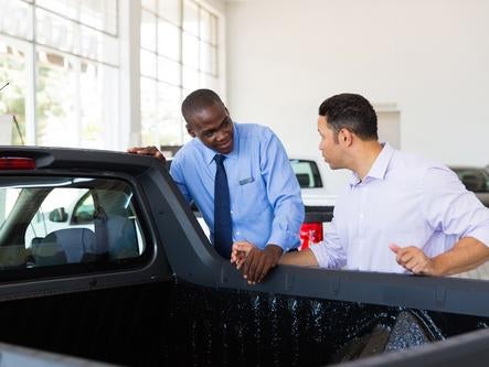 confident car salesman selling a car to middle aged customer