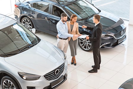 Top view photo of young male consultant and buyers signing contract for new car in auto show. Concept for car rental