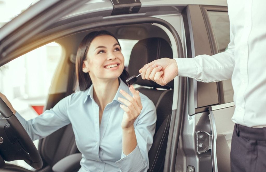Person handing a car key to a woman behind the wheel