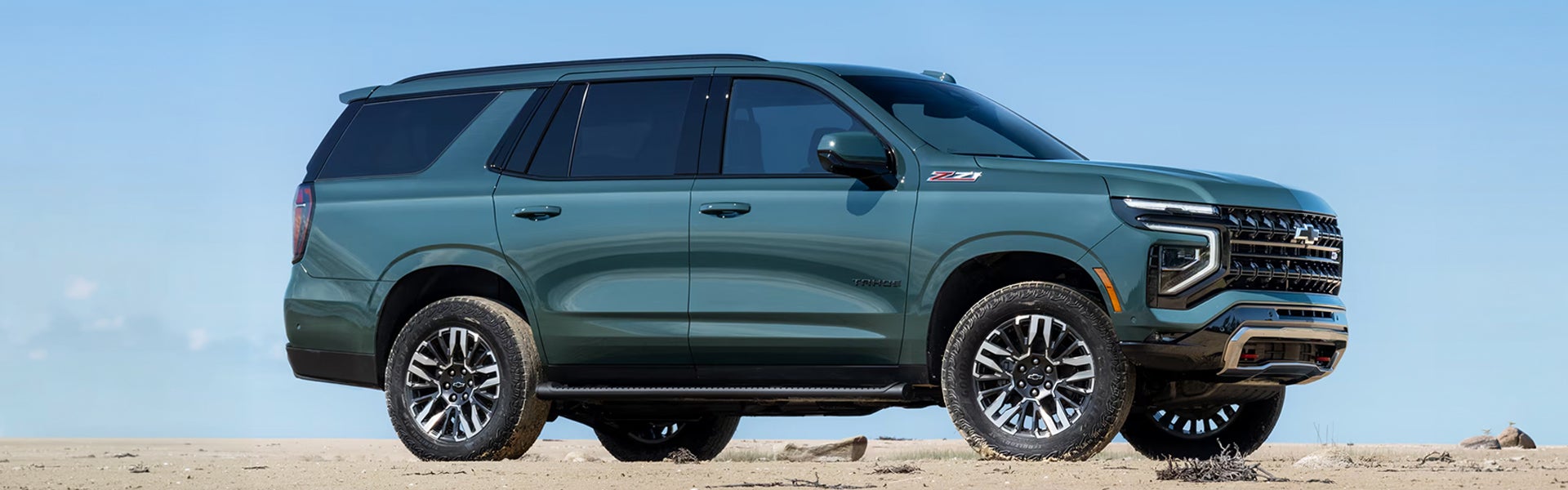 2026 Chevrolet Tahoe in blue-green parked on a sandy terrain with clear blue sky.