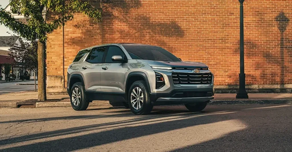 The image features a 2026 Chevrolet Equinox parked on an urban street with a brick wall backdrop. The sleek silver SUV's modern design stands out with sharp lines and a refined front grille.