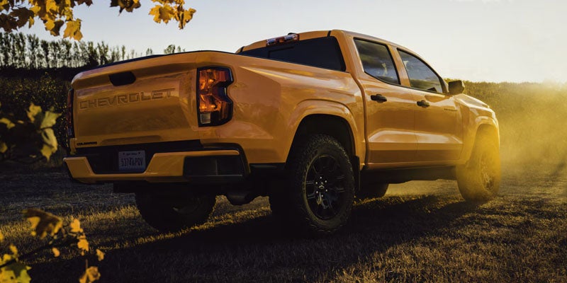 A yellow pickup Chevrolet Colorado ZR2 Bison on a dirt road at sunset, surrounded by autumn leaves. The scene conveys ruggedness and adventure with a warm, golden glow.