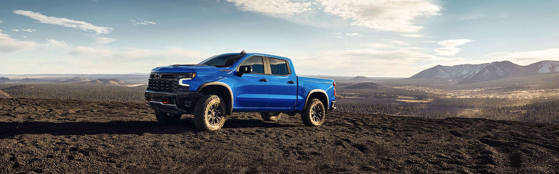 2025 Chevrolet Silverado 1500 blue pickup truck parked on a rugged off-road landscape with mountains in the background