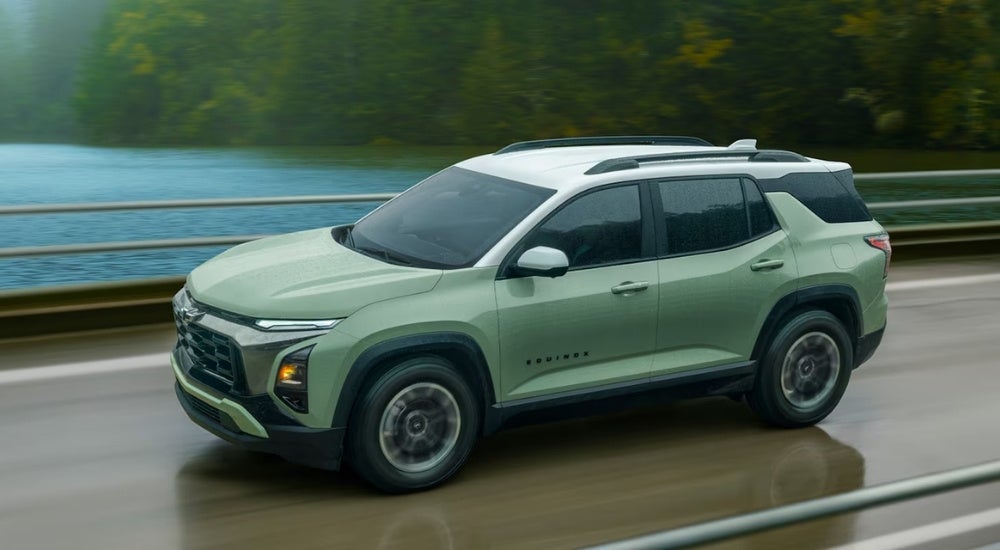 A green 2025 Chevy Equinox for sale near Leesville is driving over a bridge.