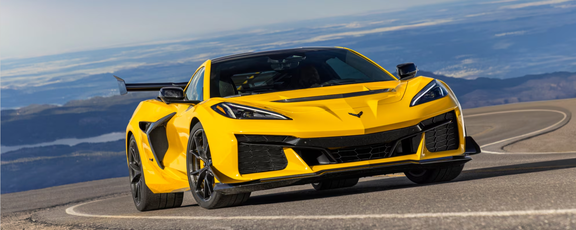 A vibrant yellow 2026 Chevrolet Corvette ZR1 sports car on a winding road with mountains in the background.