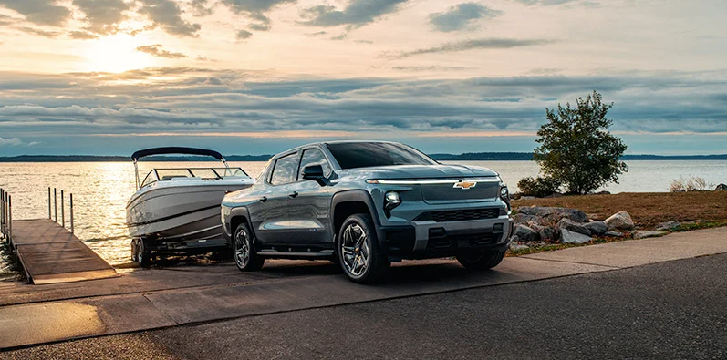 A 2026 Chevrolet Silverado EV backing up a boat down a boat ramp in to a lake.
