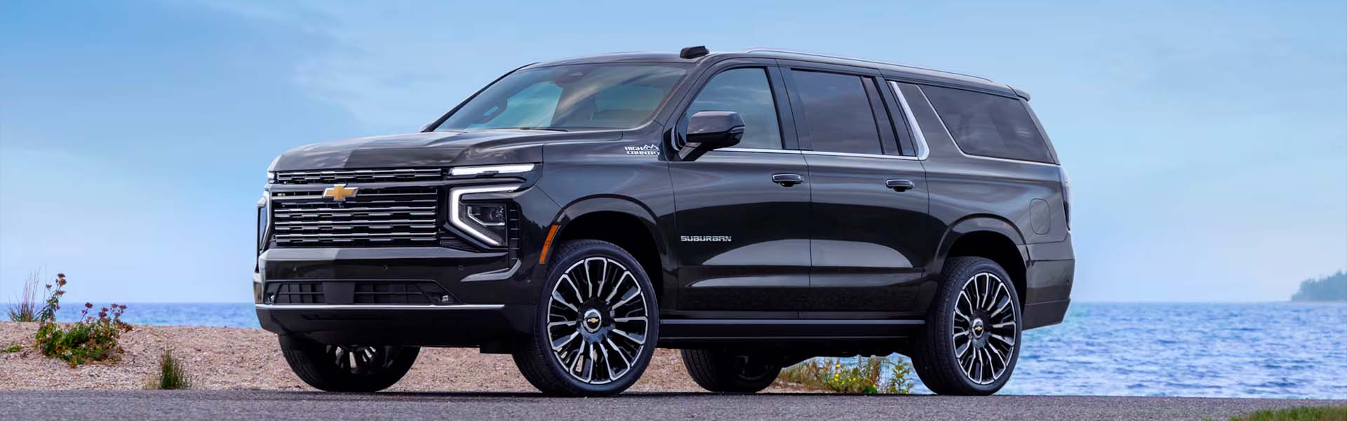 2026 Chevrolet Suburban parked by the beach, showcasing a sleek dark exterior and modern design details.