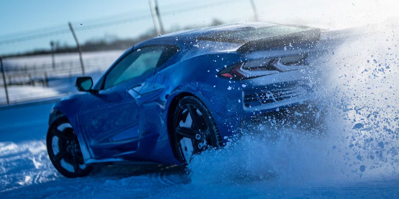 A blue 2026 Corvette E-Ray sports car driving through a snowy landscape.