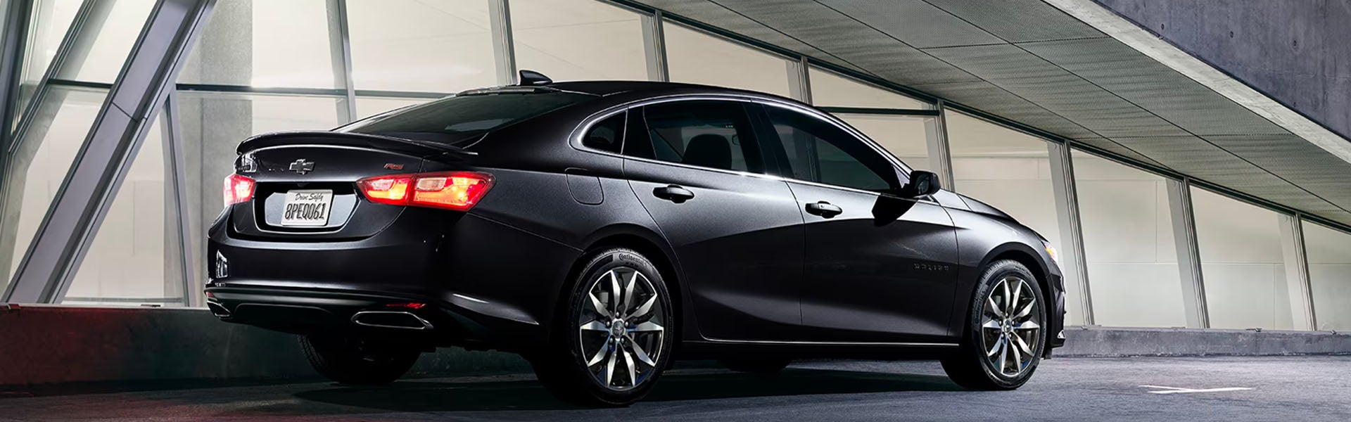 A sleek black 2025 Chevrolet Malibu sedan is parked in a modern, dimly-lit setting.