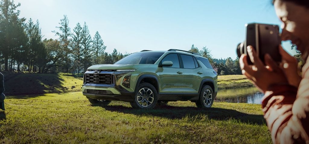 2026 Chevrolet Equinox parked in a natural landscape with trees and water, highlighting rugged exterior styling and a comfortable interior.