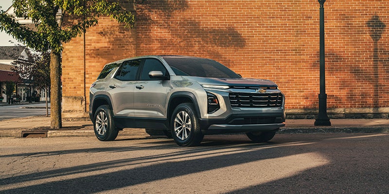 Equinox parked by a brick wall on a sunny street, under a tree with dappled shadows. The scene feels calm and suburban.