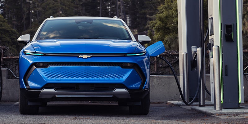 Blue Chevrolet Equinox EV plugged into a charging station.