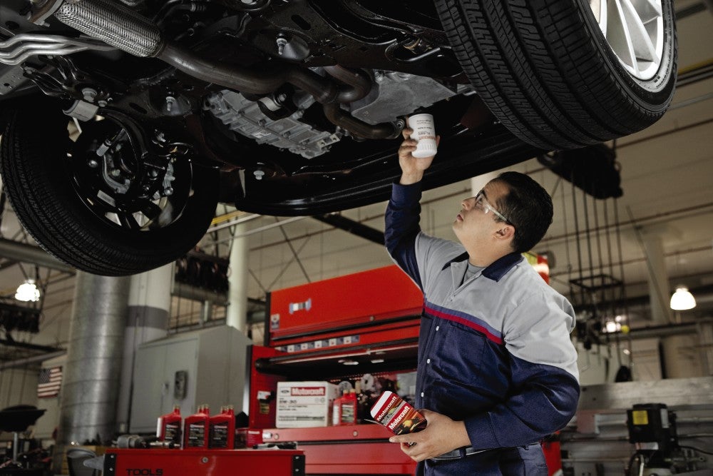 Mechanic performing an oil change on a lifted vehicle.