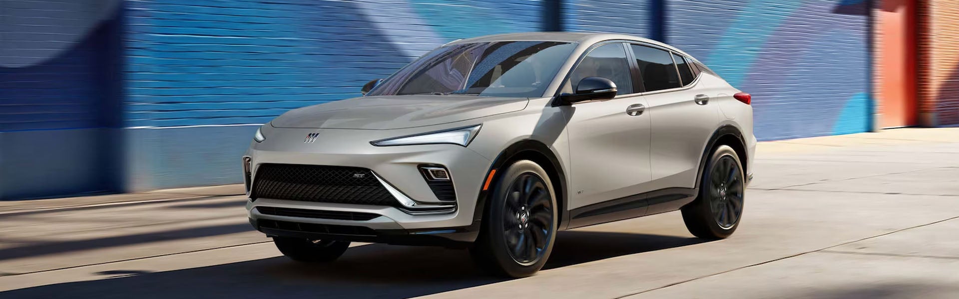 2026 Buick Envista compact SUV driving in urban setting with sleek coupe-inspired design and black wheels