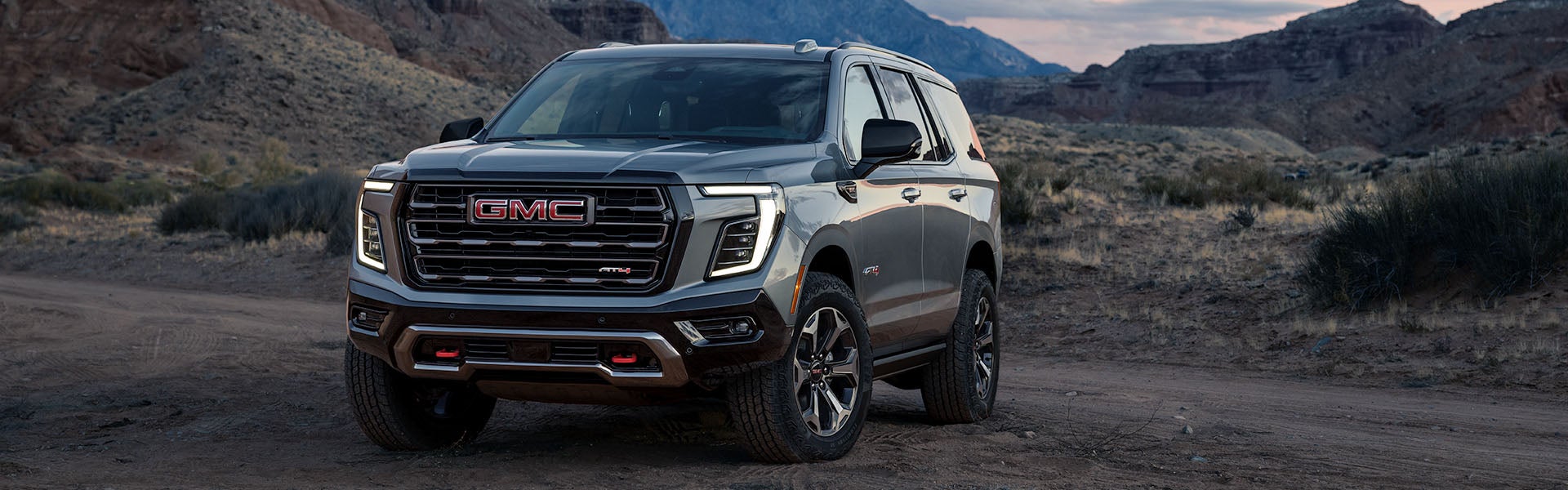 A 2026 GMC Yukon AT4 parked on a dirt road with rocky hills in the background.