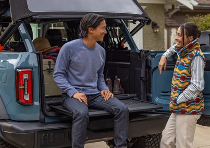 Two people smiling and sitting on the open swing-gate tailgate of a 2026 Ford Bronco Big Bend.