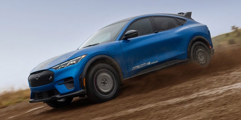 Blue Ford Mustang Mach-E Rally driving along a dirt path.