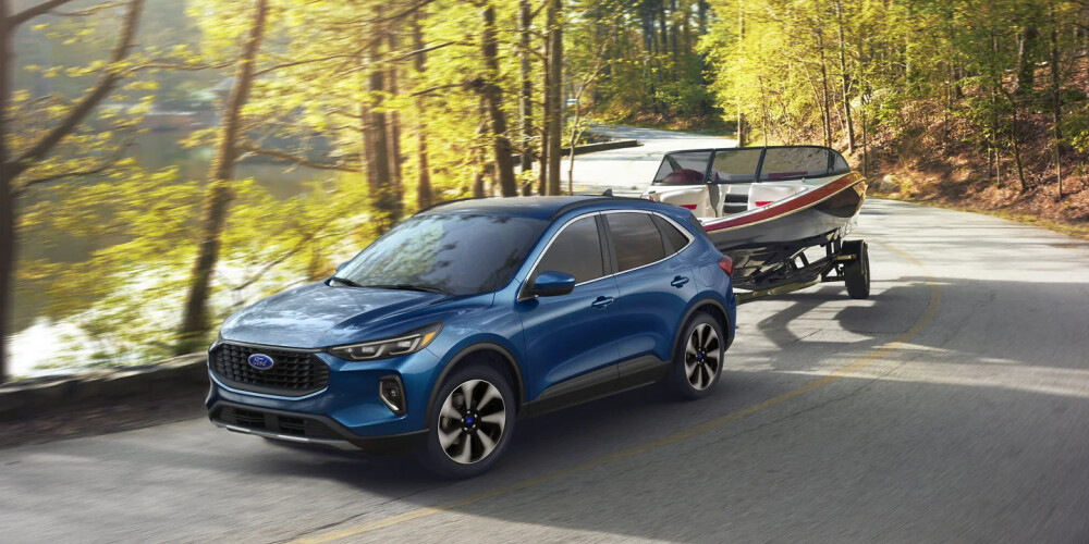 Blue SUV towing a speedboat on a winding, tree-lined road by a calm lake, under warm, golden sunlight, evoking a sense of adventure and freedom.