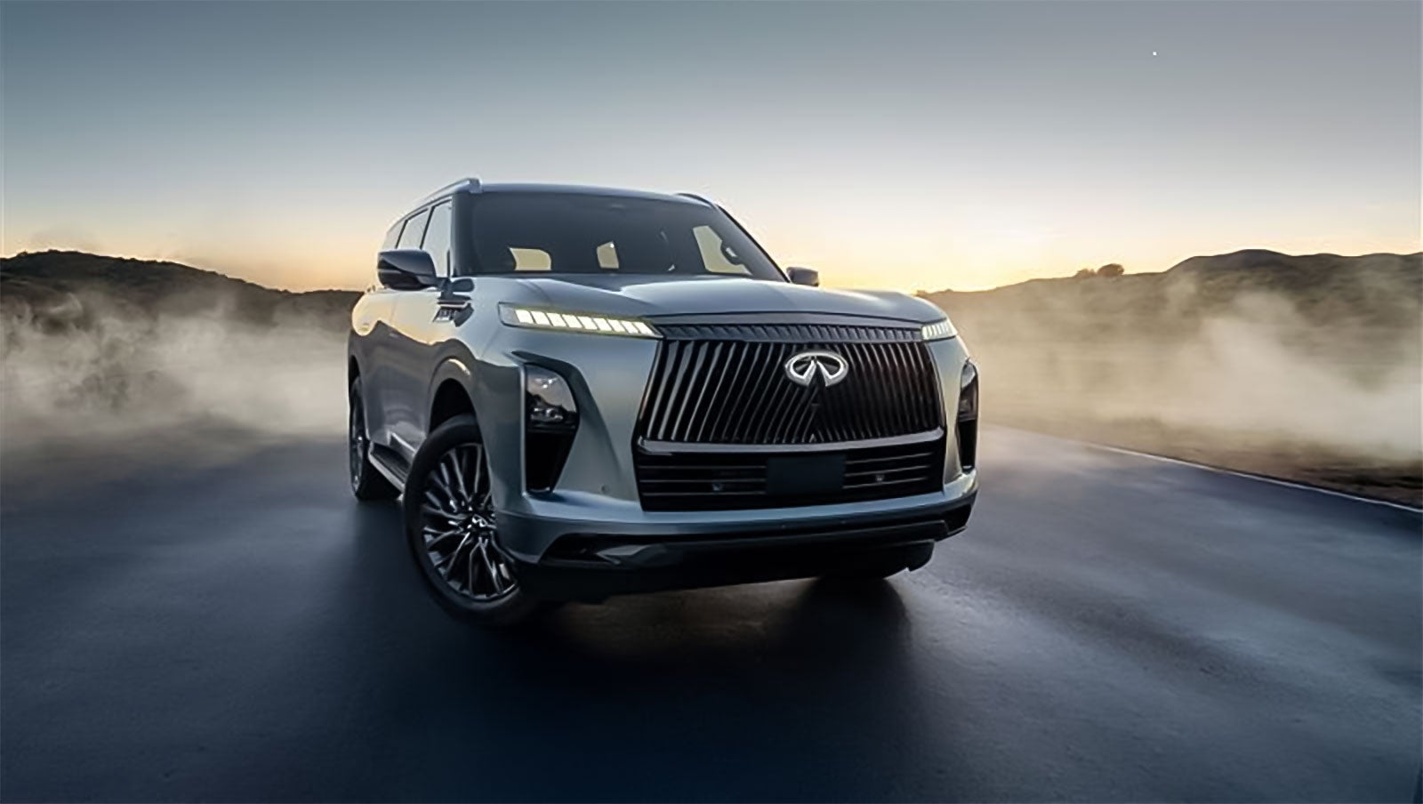 A silver Infiniti SUV on a road at dusk, with mist surrounding the vehicle