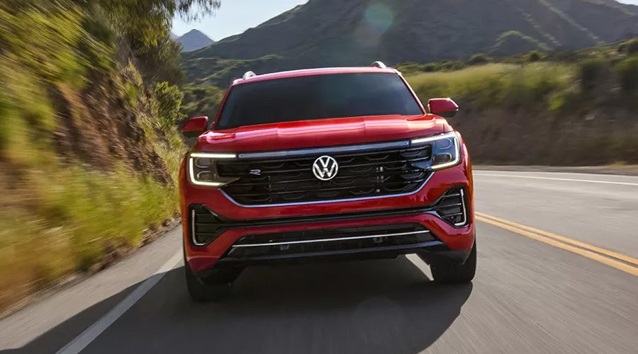 A red Volkswagen Atlas SUV driving on a scenic road surrounded by hills, showcasing its bold front grille and sleek design