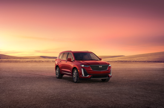 A red SUV is parked on a vast desert landscape under a vibrant, pink-orange sunset sky. The scene conveys a sense of adventure and tranquility.