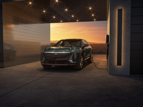 Electric car charging in a modern garage at sunset. The vehicle is parked under a sleek structure with warm lighting, against a serene orange sky.