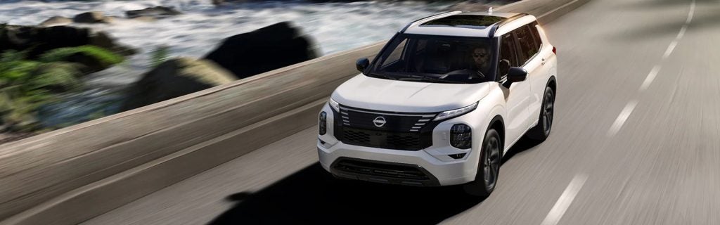 White Nissan SUV driving along a coastal highway.