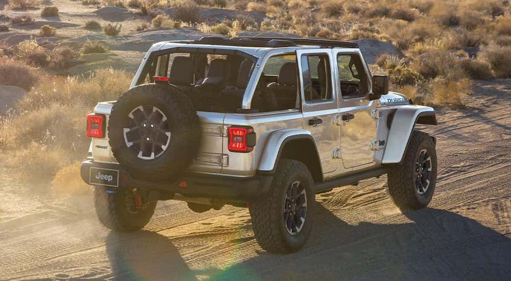 Rear view of a silver 2024 Jeep Wrangler 4xe Rubicon driving in the desert.