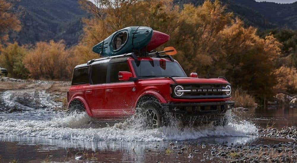 A red 2024 Ford Bronco Outer Banks driving over a shallow body of water.