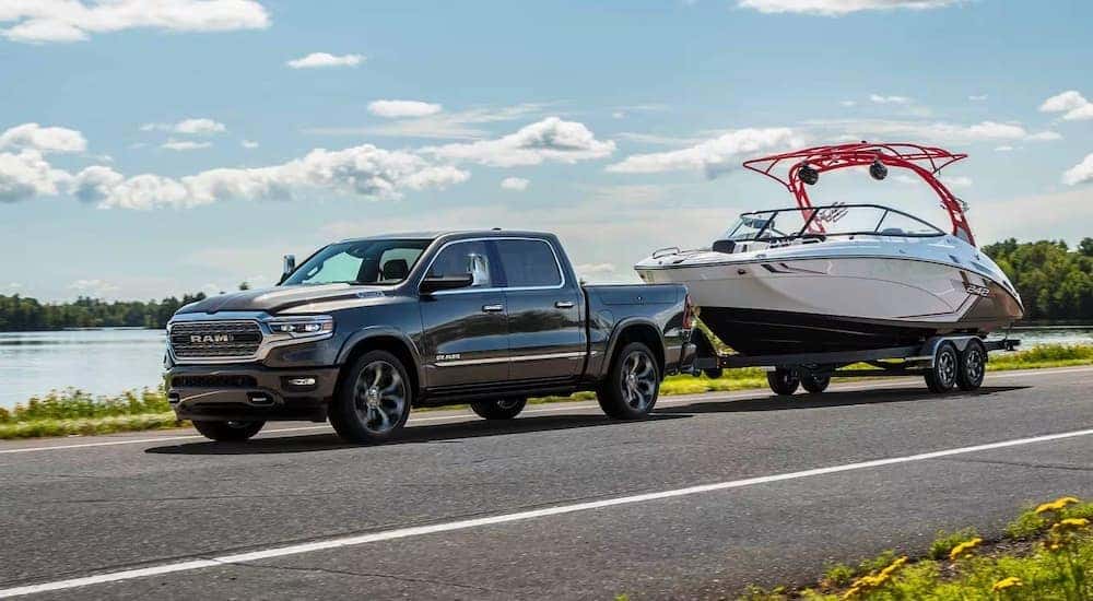 A dark gray 2024 Ram 1500 is shown towing a boat near a lake.