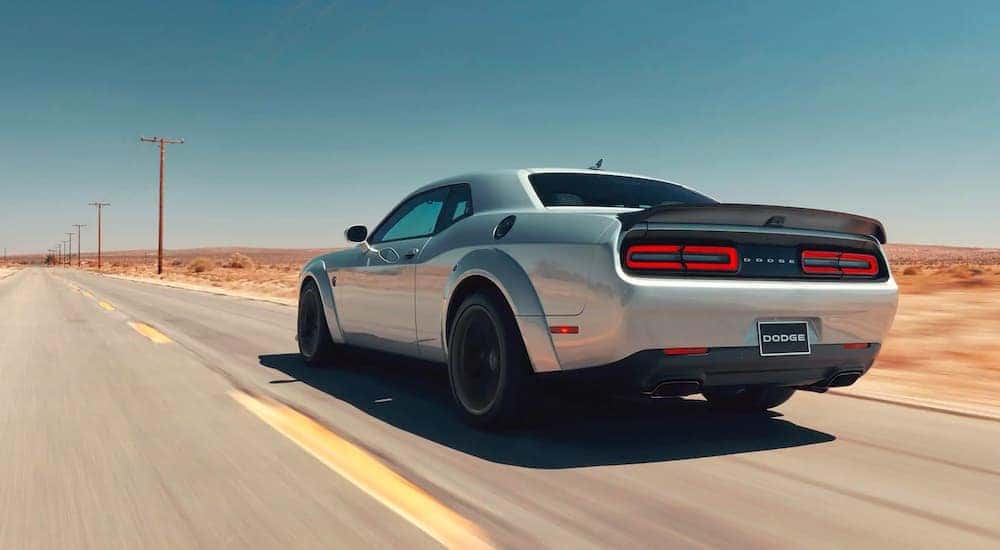 A silver 2020 used Dodge Challenger is shown from the rear driving down a deserted road.