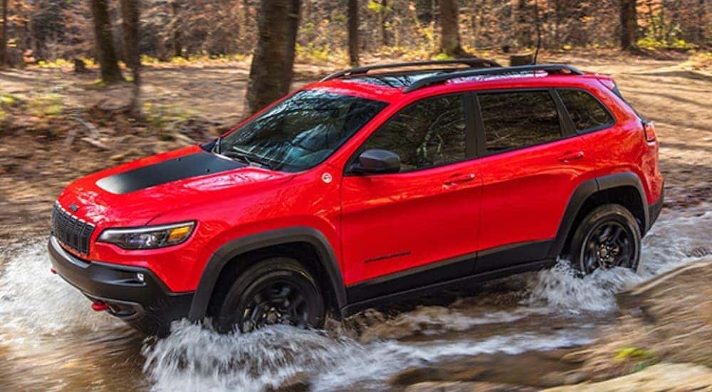 A red 2020 Jeep Cherokee is crossing a river while off-roading.