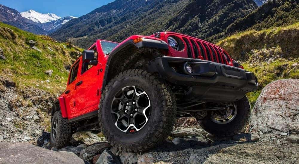 A red 2024 Jeep Wrangler Unlimited driving over rocks after visiting a dealer with a Jeep Wrangler for sale near Independence.