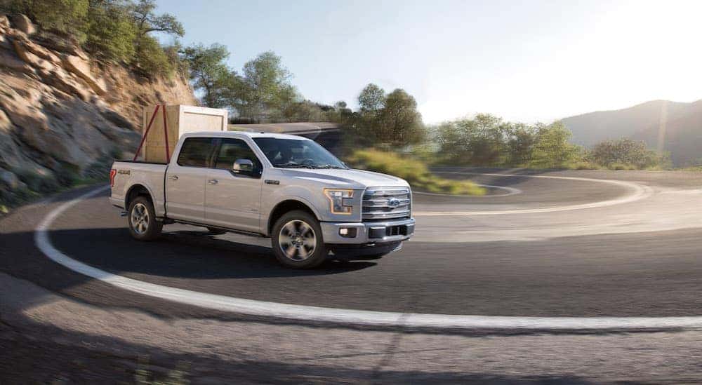 A white 2015 Ford F-150 is hauling a crate around a corner.