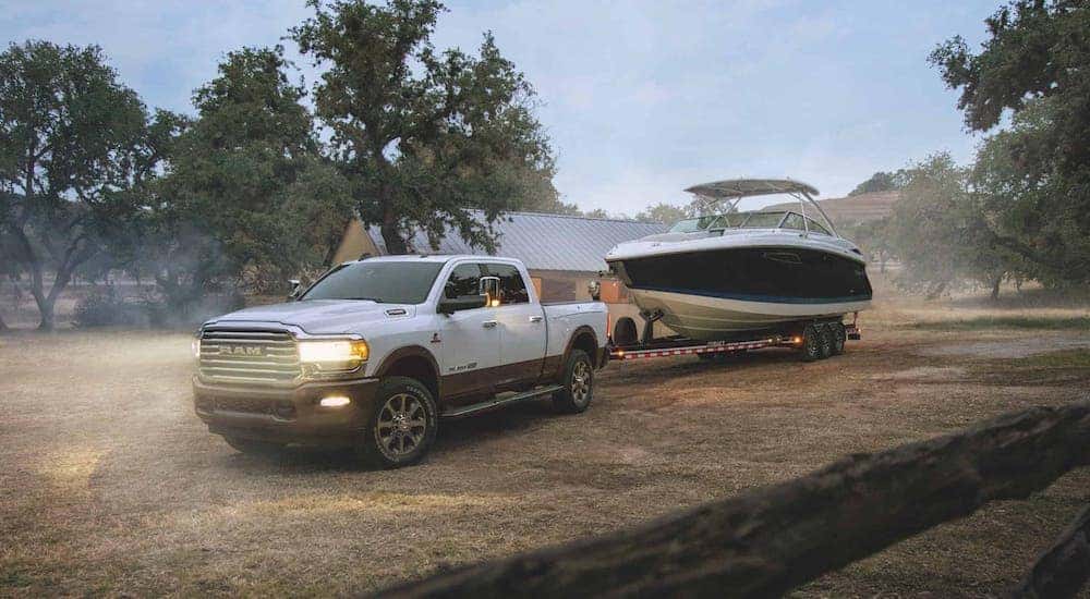 A white 2018 used Ram 2500 diesel is towing a boat at a ranch.