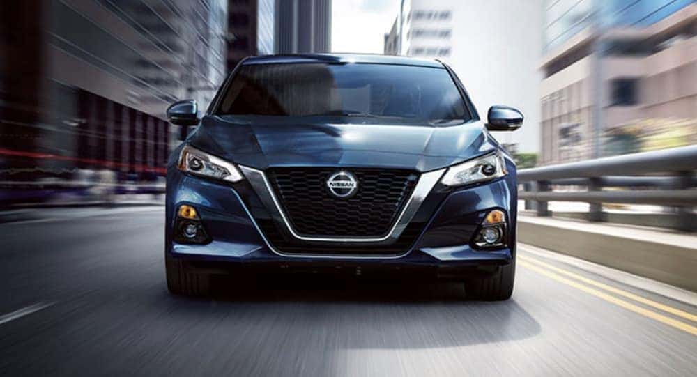 A blue 2020 Nissan Altima is shown from the front driving through a city after leaving a Lexington used car lot.