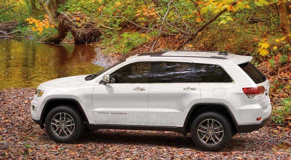 A white 2020 Jeep Grand Cherokee, popular among new vehicles for sale, is parked on a rocky river bank.