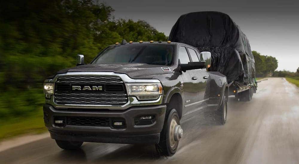 A black 2020 Ram 3500 HD is shown towing a trailer on a rainy road. 
