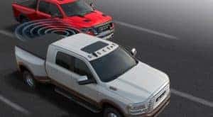 A white 2020 Ram 3500 is shown with simulated blind spot monitoring sensor line next to a red Ram 1500 TRX.