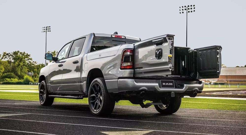 A silver 2024 Ram 1500 is shown from the rear at an angle with the tailgate open after leaving a dealer that has a Ram 1500 for sale.