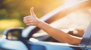 A person is holding their hand out of a car window giving a thumbs up after leaving a bad credit car dealership.